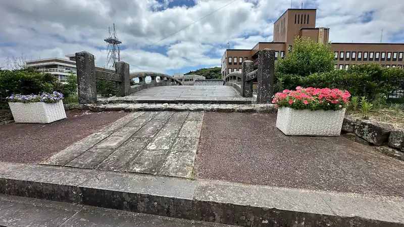 長崎県平戸市にある江戸時代築造の石橋、幸橋の上から見た景色。石畳の橋の両側に花が飾られ、背景に現代的な建物が並ぶ風景