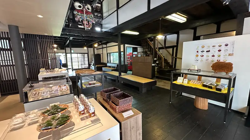 長崎県平戸市の按針の館一階にある和菓子販売と飲食スペース。土産品が並ぶ棚やテーブル、伝統的な木造の内装が見える