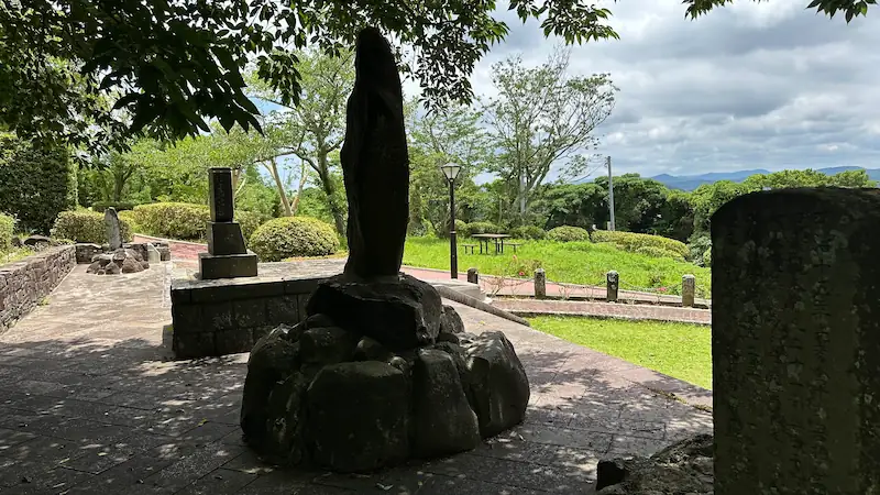 三浦按針の墓所に立つ石像を後ろから撮影。木々の間から見える芝生と遊歩道が広がる静かな風景
