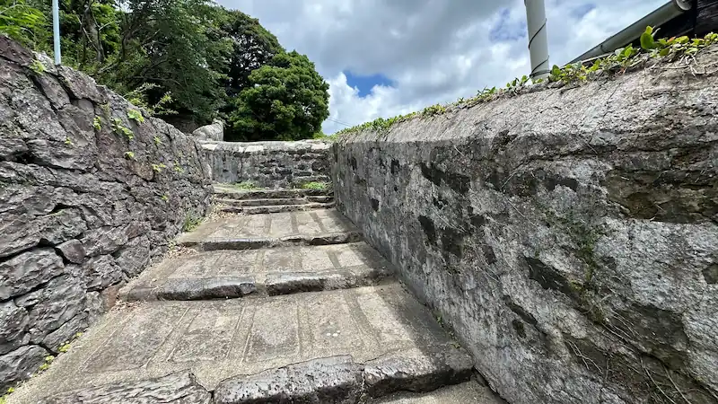 平戸市に残るオランダ塀沿いの石段を下から見上げた写真。石造りの塀と階段が青空に映える