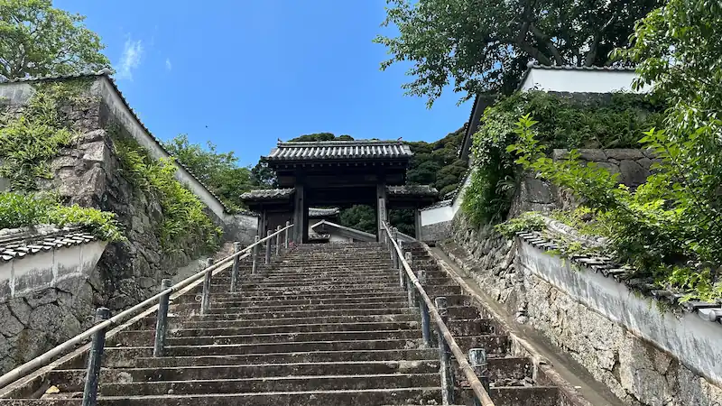 長崎県平戸市にある松浦史料博物館の正面。石段の上に門が立ち、白壁と石垣が続く歴史的な建物