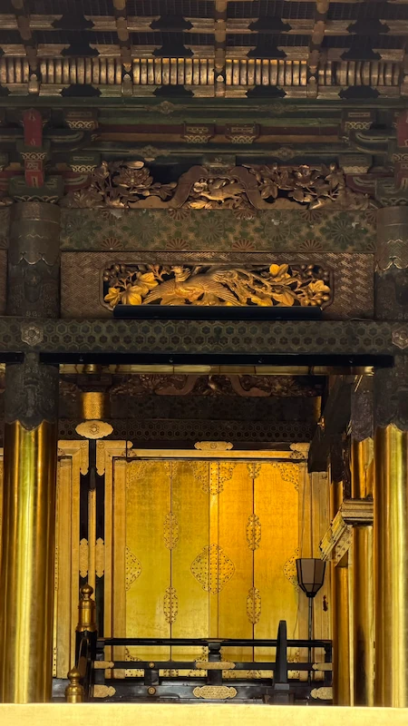 Interior of Ueno Toshogu Shrine’s Kinshikiden. Golden inner doors and carvings are visible. Warm gold glows within the dim space.