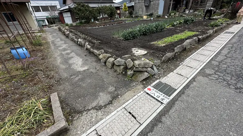 A sign reading 'Entrance: site traditionally identified as Akechi Mitsuhide's residence,' with a narrow path continuing past farmland beyond it.