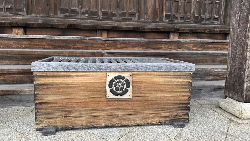 A wooden offertory box in front of a hall at Jogon-in Temple, bearing the Oda clan's mokko (melon) crest on its face.