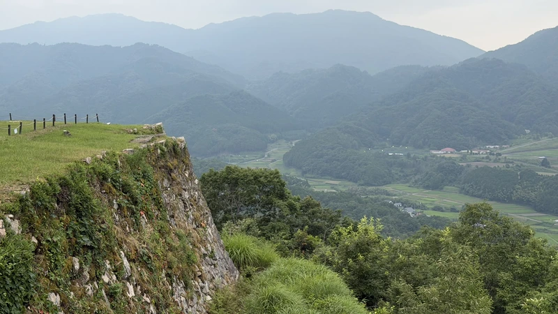 View from the edge of the stone wall at Kita-Senjo, looking over a valley and mountains, showing how the bailey sits along the mountain ridge.