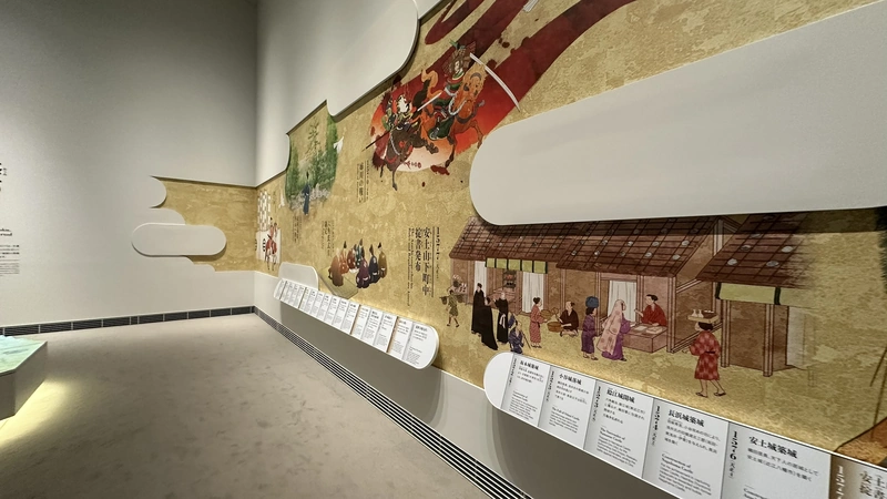 A museum gallery lined wall-to-wall with illustrated maps and explanatory panels about Azuchi Castle and its surrounding castle town.