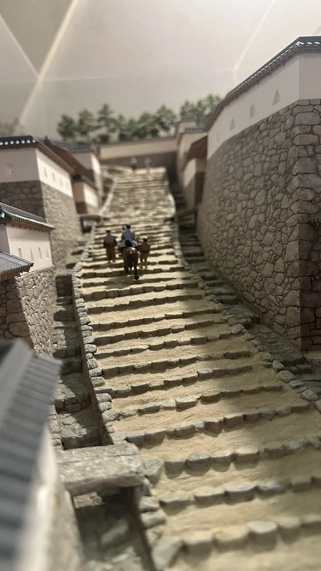 A reconstructed model of Azuchi Castle's Otemichi approach, flanked by stone walls, with miniature figures climbing the wide stone stairway.