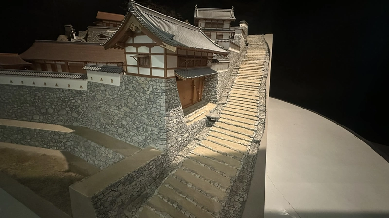 A three-dimensional model recreating the stone walls and buildings around Azuchi Castle's Otemichi approach, showing the slope of the stairway and building layout from the side.
