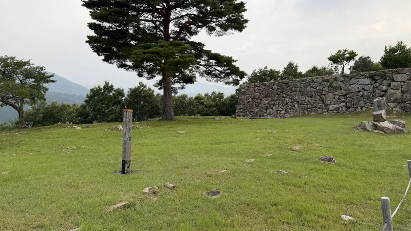 The wide lawn, stone walls, and a signpost at Minami-Senjo, giving a sense of the scale of the bailey and the mountains around it.