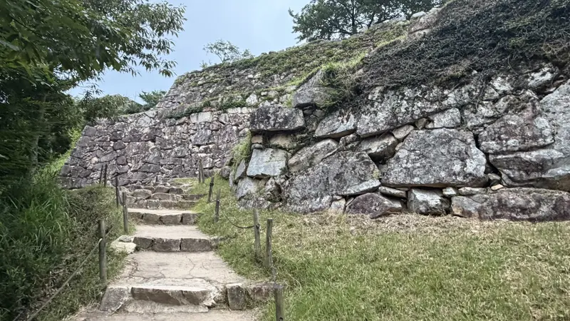 Stone steps beside a tall stone wall near Mitsuke Turret Site, with the viewing path bending alongside the wall.