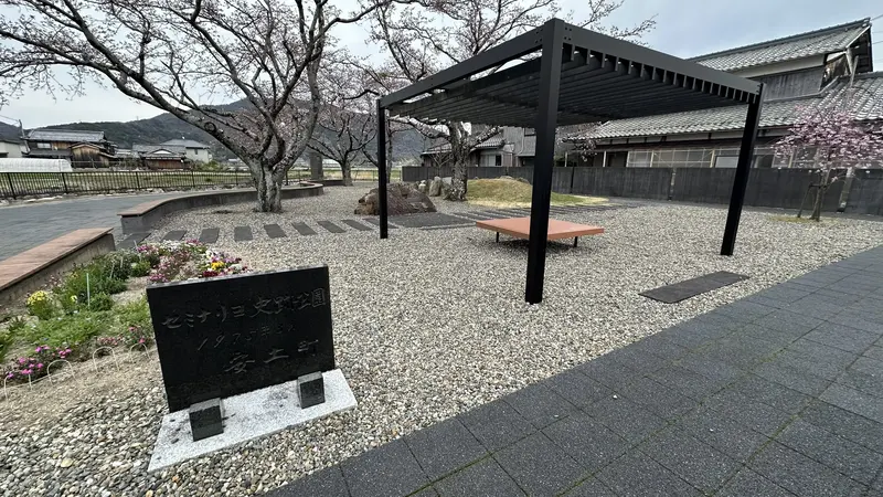 A stone monument and rest area at the Seminario Historic Site Park, set within a plaza surrounded by cherry trees and flower beds.