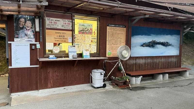 The ticket booth at the entrance to Takeda Castle Ruins, with signage showing opening hours and other visitor information.