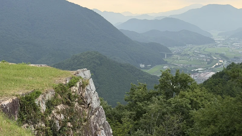 View looking down over the Takeda valley and surrounding mountains from the upper part of the ruins, with the stone wall edge of a bailey visible.