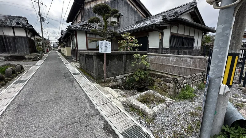 A narrow lane through the Azuchi neighborhood leading to the 'Ume-no-kawa' water spot, with stonework remains beneath an information sign.