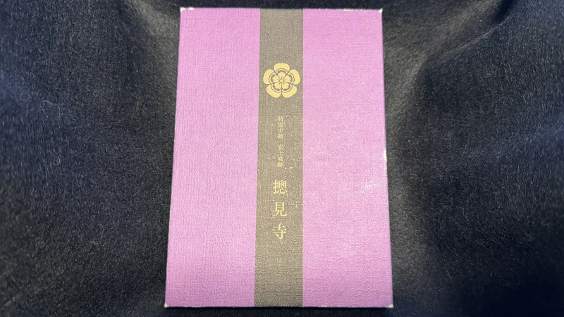 黒い布地の上に置かれた、紫色と黒色の摠見寺の御朱印帳。中央には金色の織田木瓜紋と「特別史跡 安土城跡 摠見寺」の文字が入っている。