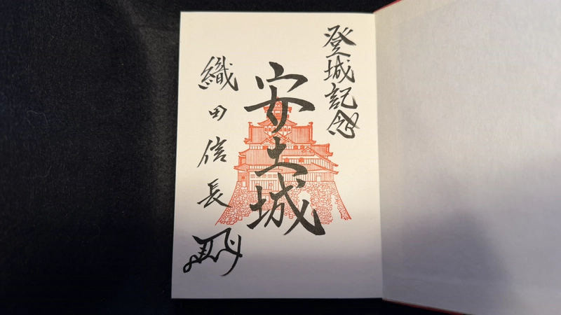 開いた御朱印帳に記された安土城登城記念の墨書。赤色で描かれた安土城の図の上に大きく「安土城」と書かれ、左側には織田信長の名が添えられている。