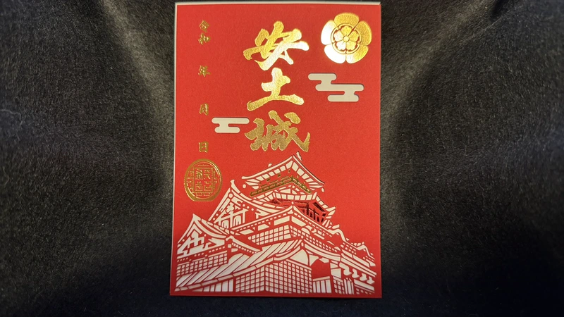 赤い台紙に金色の「安土城」の文字、織田木瓜紋、城郭の図を配した登城記念の御城印。左側には年月日を書き込む欄が設けられている。