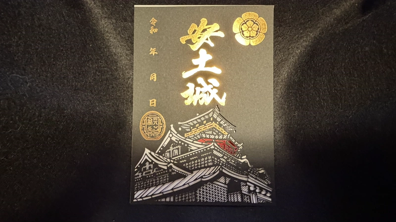 黒い台紙に金色の「安土城」の文字と織田木瓜紋、白・金・赤で表現した城郭の図を配した登城記念の御城印。左側には年月日欄がある。