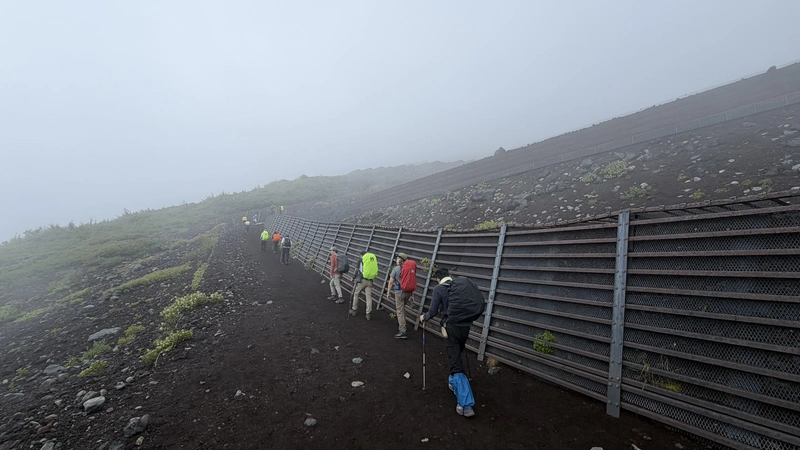 高い防護柵に沿って登る火山砂礫の道