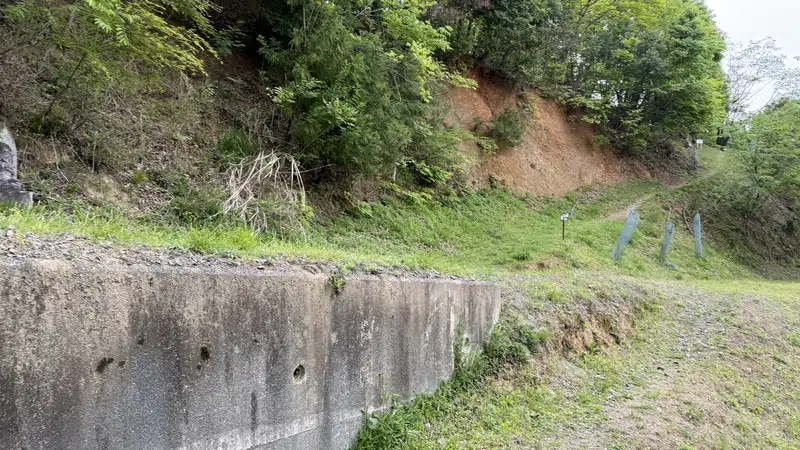 A path running alongside a retaining wall at the foot of the mountain