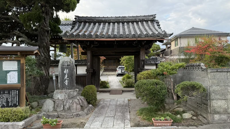 A front view of Chokoji Temple's gate. A stone marker engraved with the temple's name and an information board stand in front of it.