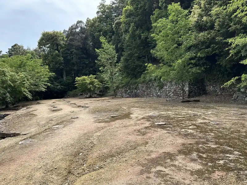 Foundation stones scattered across the terrace at the residence ruins traditionally attributed to Hideyoshi, with stone walls continuing in the background.