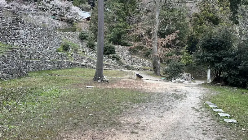 The lower terrace at the residence ruins traditionally attributed to Hideyoshi, with stone steps and multiple tiers of stone walls visible among the trees.