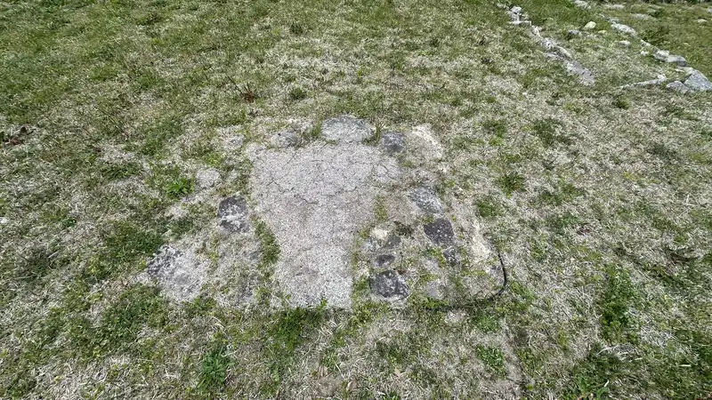 A circular stone-lined remain at ground level, with rows of stones marking building foundations extending around it.