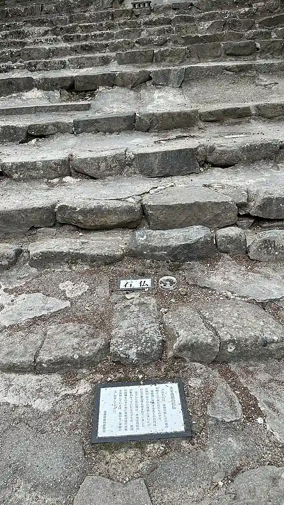 A stone Buddha statue repurposed as a paving stone in Otemichi's stairway, photographed from above alongside a small information sign explaining its origin.