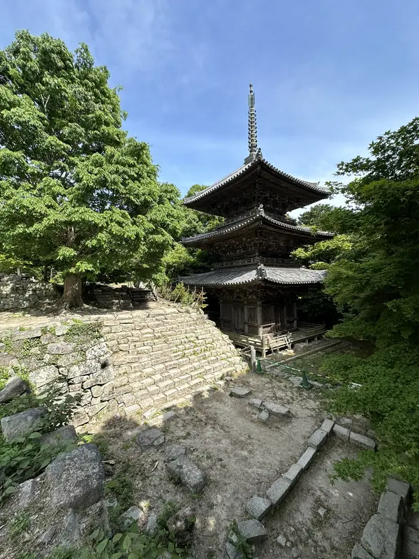A vertical view of the Three-Story Pagoda looking up from below the stone wall, with the stone steps and full height of the pagoda in frame.