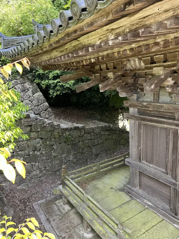 A side-angle close-up of the ground floor of the Three-Story Pagoda and the stone wall, showing the bracketing and veranda structure.