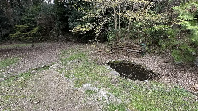 A flat terrace at the residence ruins attributed to Takei Sekian, with the stone-lined remains of a water feature and a wooden structure at one edge.