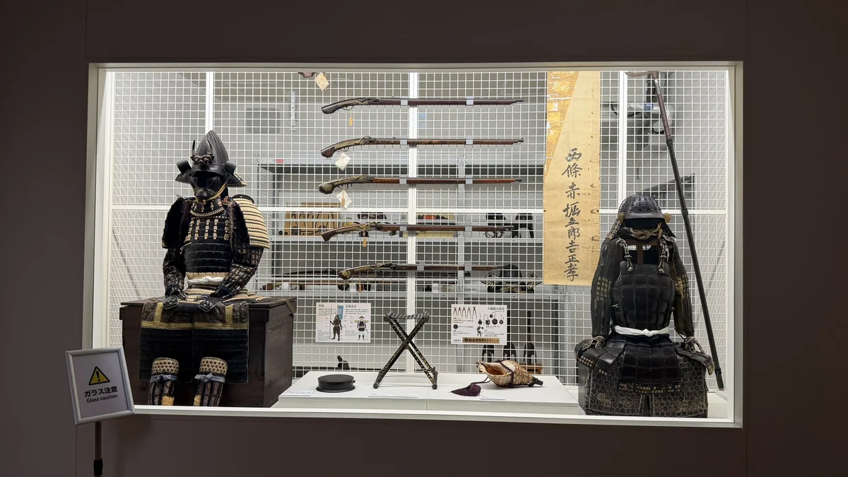 Two suits of armour displayed with matchlock guns and spears in the visible storage room