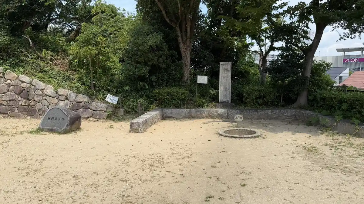 Open ground at Arioka Castle with the well, a stone monument and a stone wall
