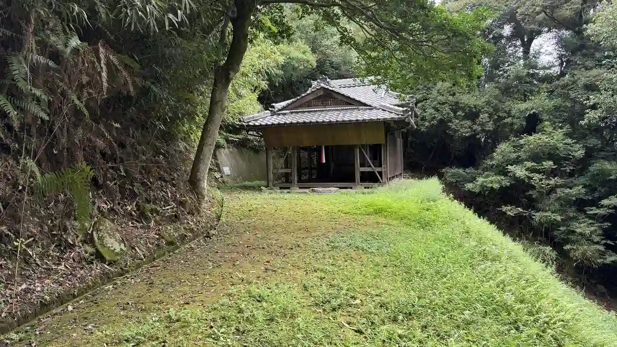 林の奥に建つ木造の社殿を正面から見た様子。屋根と入口の開口部が見えます。