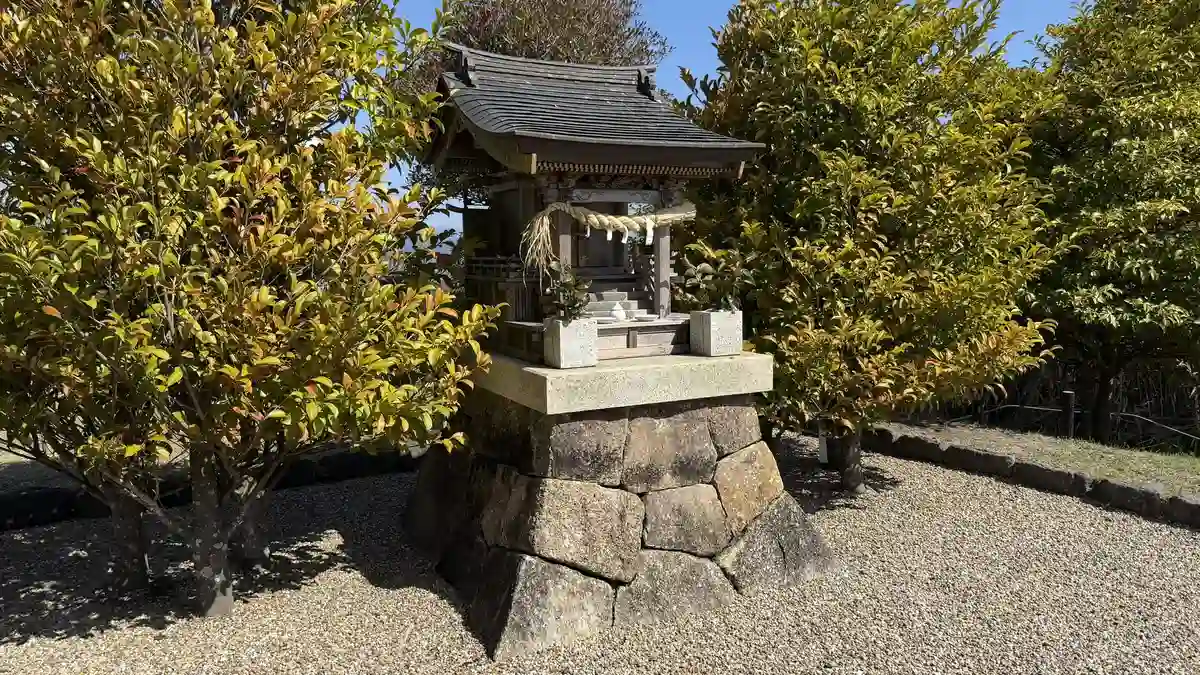 A small shrine in the Nihondaira Hotel garden, a wooden building hung with a sacred rope on a stacked-stone plinth