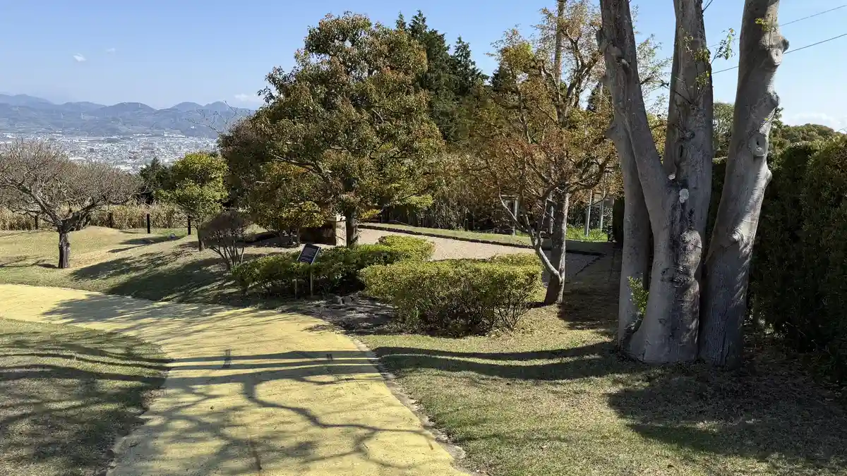 A gravel path across the Nihondaira Hotel lawn garden, with the information board and shrine among trees and the town visible in the distance
