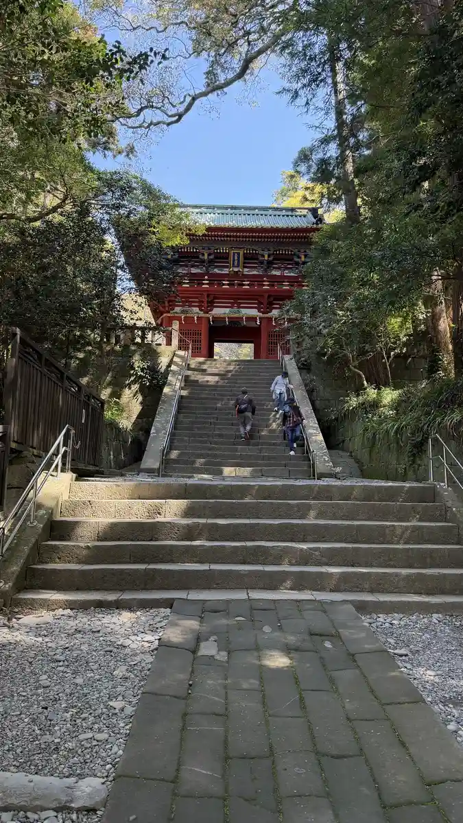 The vermilion two-storey Romon gate of Kunozan Toshogu appearing at the top of a stone stairway between trees