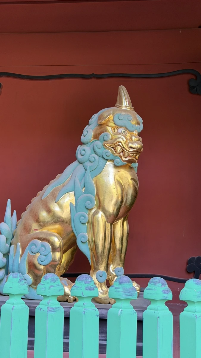 A guardian lion figure painted gold and blue inside the vermilion Romon gate