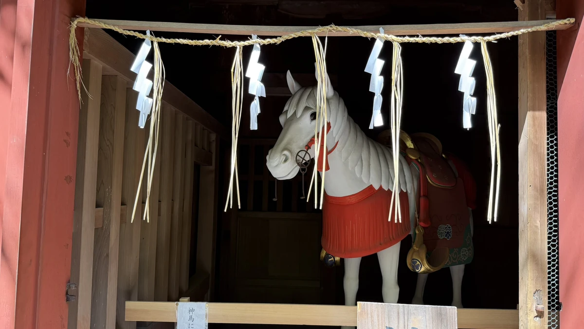 A white wooden horse figure with a straw rope inside the sacred stable at Kunozan Toshogu