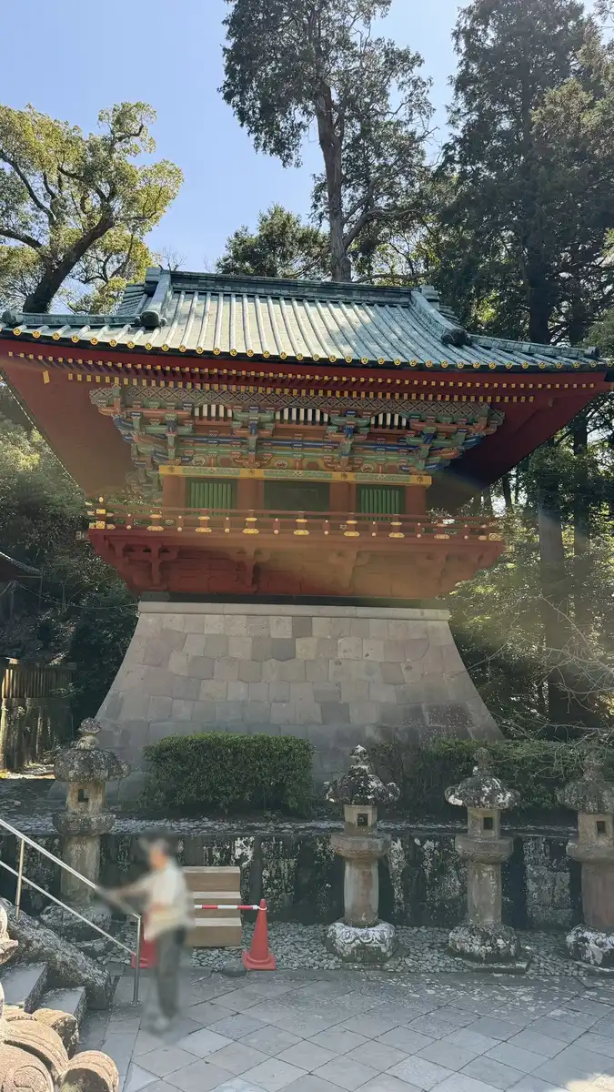The two-storey vermilion drum tower above stone walling in the precinct of Kunozan Toshogu (image edited to obscure a person)