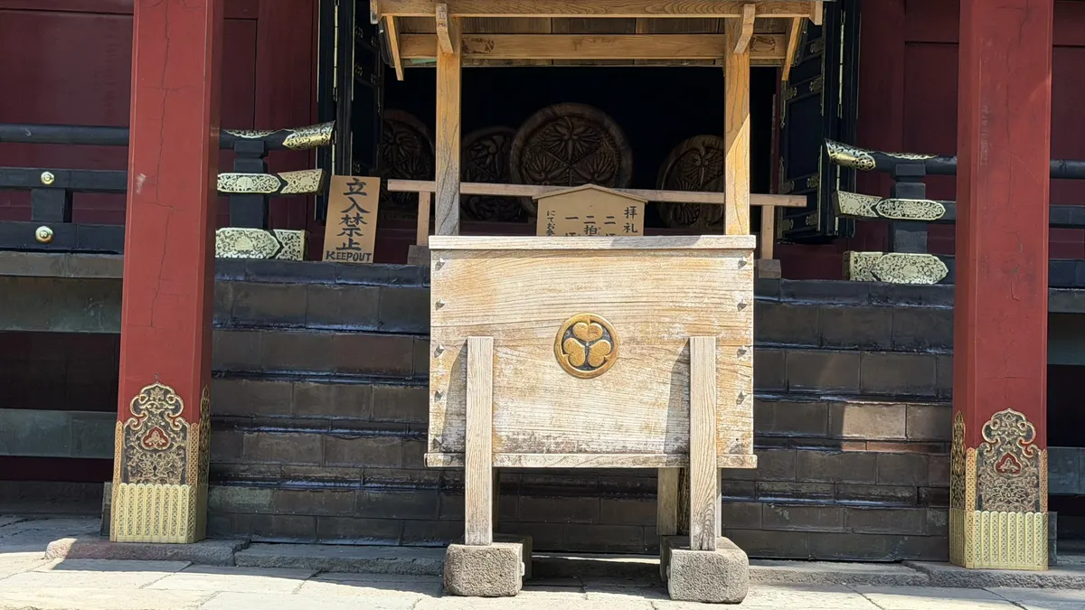 The front of Hie Shrine with an offertory box bearing the triple hollyhock crest