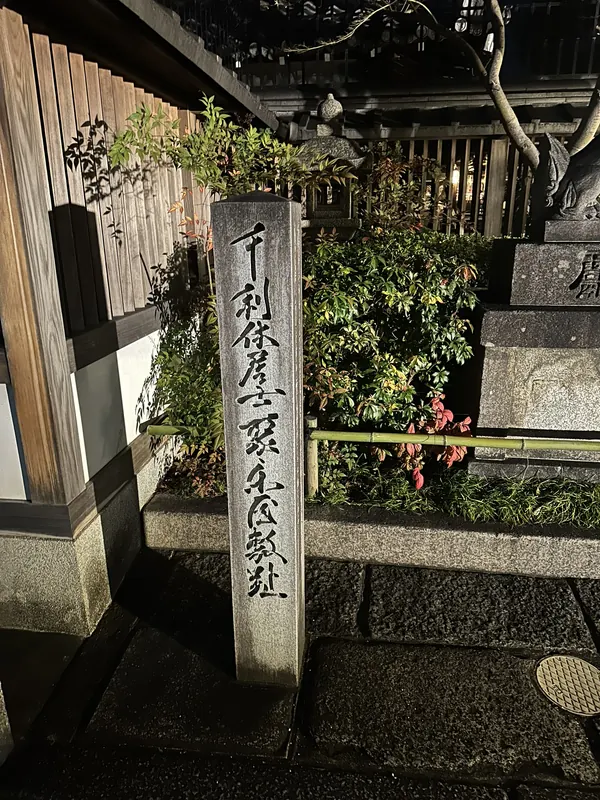 「千利休居士聚楽屋敷趾」と刻まれた石標。石垣と植込みを背に立つ
