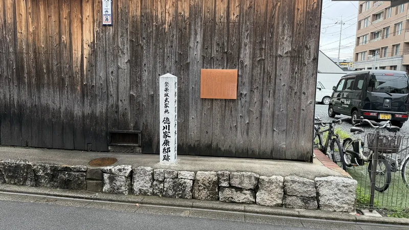 「聚楽城 武家地 徳川家康邸跡」と刻まれた石標。木造の壁を背に立つ