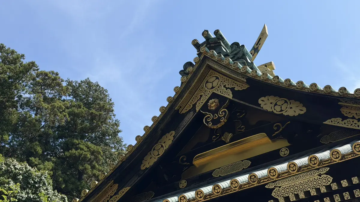 The roof edge and a hollyhock crest of the shrine buildings against a blue sky