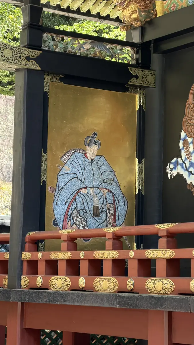 A black fitting painted with human figures beside a red railing at Kunozan Toshogu