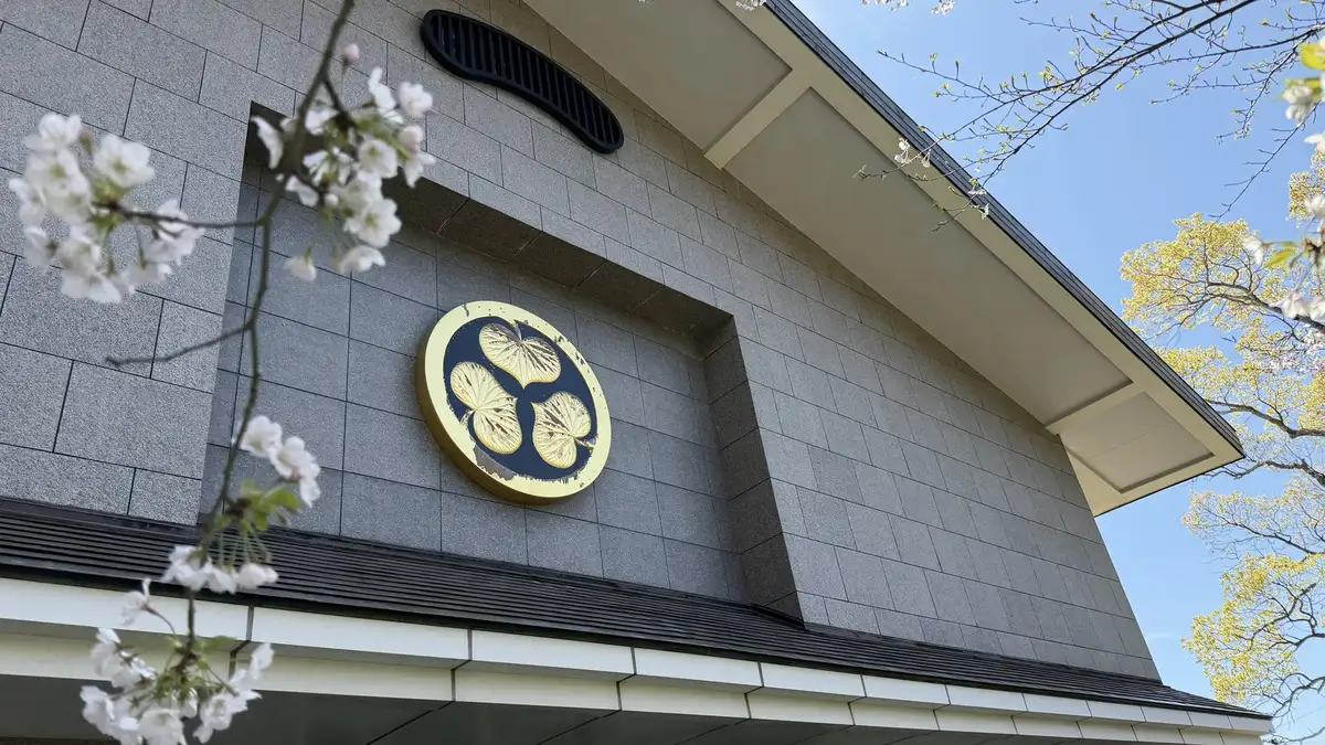 The wall and crest of the Kunozan Toshogu Museum seen beyond flowering cherry branches