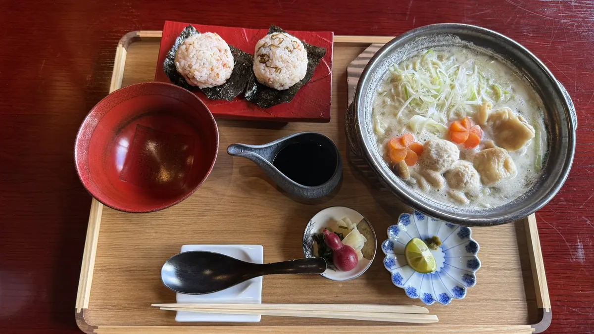 Mizutaki ramen in a clay pot with rice balls and pickles on a tray