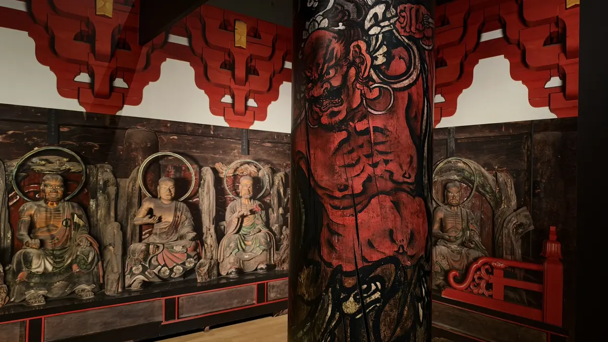 A recreated pillar painting of a red guardian king, with arhat photo panels behind it