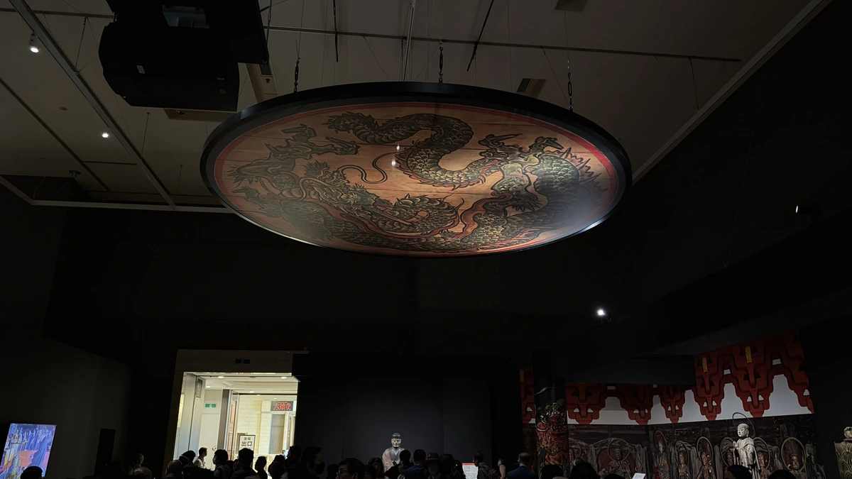 A circular reproduction of the gate’s dragon ceiling painting suspended above exhibition visitors